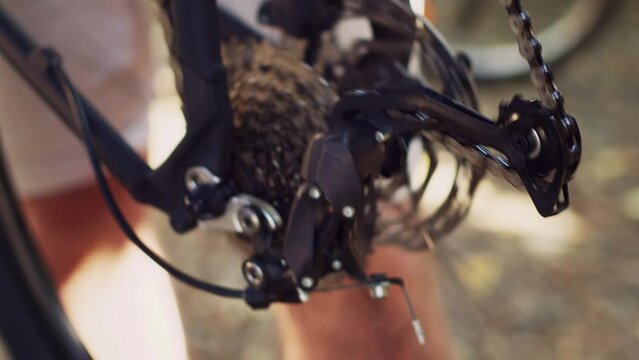 Healthy caucasian male examining broken bike wheel chain ring with professional equipment in home yard. Close-up view of servicing of bicycle by young man for outdoor summer cycling.