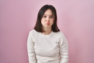 Fototapeta premium Woman with down syndrome standing over pink background looking at the camera blowing a kiss on air being lovely and sexy. love expression.
