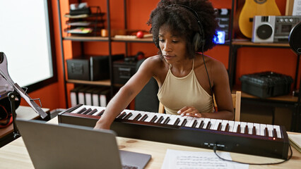 African american woman musician playing piano using laptop at music studio