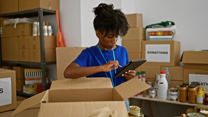 African american woman volunteer using touchpad checking products on package at charity center - obrazy, fototapety, plakaty