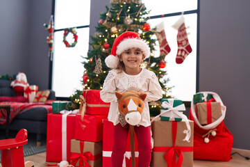 Obraz na płótnie Canvas Adorable hispanic girl playing with reindeer rocking by christmas tree at home