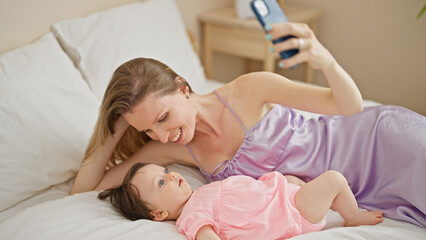 Obraz na płótnie Canvas Mother and daughter lying on bed make selfie by smartphone kissing at bedroom