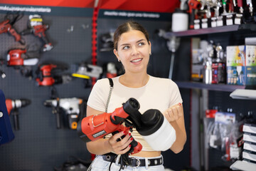 Fototapeta na wymiar Woman chooses and buys paint spray gun in a hardware store