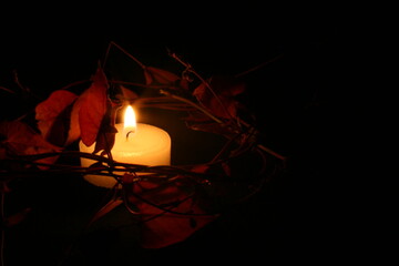 A flickering candle illuminates the darkness as it stands amidst fallen leaves.