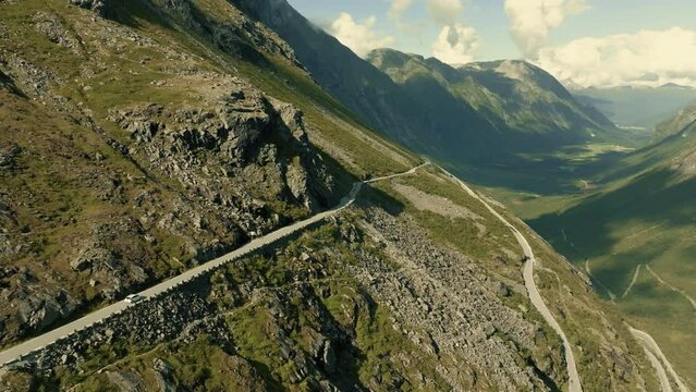 Epic panorama of a Trollstigen mountain road with cars driving and stunning fjord landscape in the background.