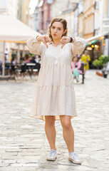 Dislike. Upset young woman showing thumbs down sign gesture, expressing discontent, disapproval, dissatisfied bad work, mistake. Displeased lovely girl walking in urban city street outdoors. Vertical