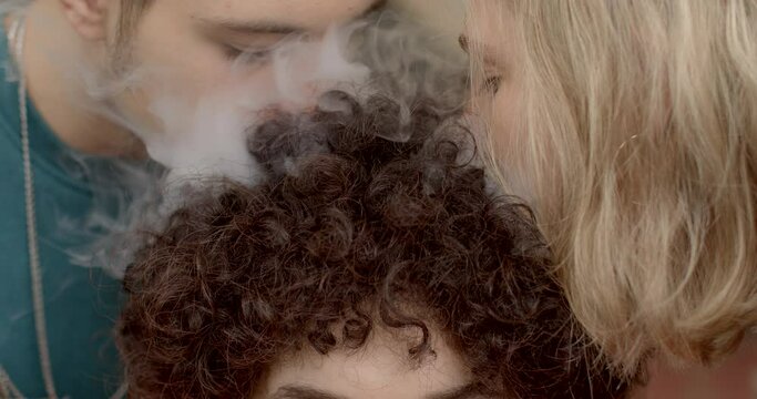 Closeup blowing smoke at person curly hair close up. Manipulating friendships. Students demonstrate arrogance in communication. Bullying in college university environment campus bullying. 