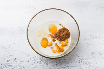 Glass bowl with milk, eggs, pumpkin puree, spices on a light blue table, top view. Stage of preparing homemade pumpkin croutons