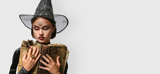 Obraz premium Young witch with spell book on light background with space for text