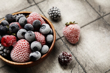 Bowl of frozen berries on grunge tile background