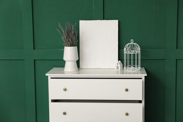 Vase with lavender and painting on white chest of drawers near green wall