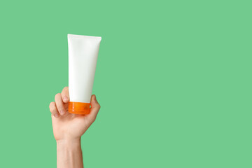 Female hand with bottle of sunscreen cream on green background