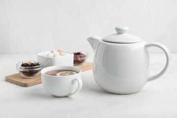 Cup of tea, teapot and sugar on light background