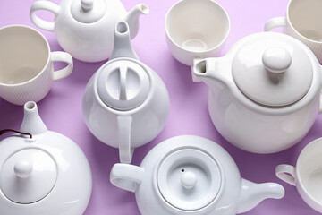 Many porcelain teapots and cups on lilac background