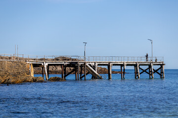 Fototapeta premium The iconic Second Valley jetty with a man fishing from the end located on the Fleurieu Peninsula South Australia taken on September 11th 2023