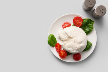 Plate of tasty Burrata cheese with basil and tomatoes on white background
