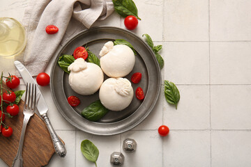 Plate of tasty Burrata cheese with basil and tomatoes on white tile table