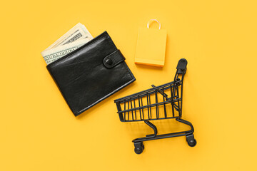 Small shopping cart, bag and wallet with money on yellow background