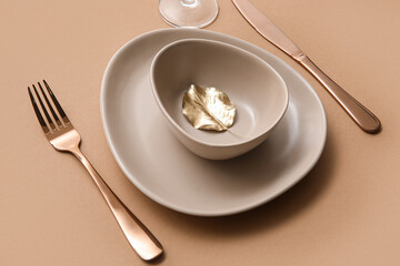 Elegant table setting with golden leaf and cutlery on brown table