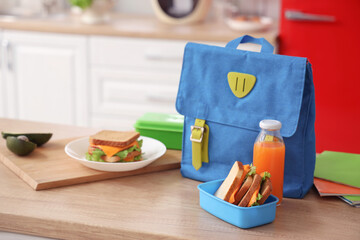 School lunchbox with sandwiches, juice and backpack on table in kitchen