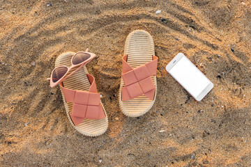 Stylish flips flops with sunglasses and mobile phone on sand at resort