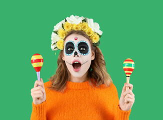 Shocked young woman with painted skull and maracas on green background, closeup. Mexico's Day of the Dead (El Dia de Muertos) celebration