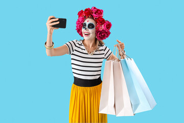 Young woman with shopping bags taking selfie on blue background. Mexico's Day of the Dead (El Dia de Muertos) celebration