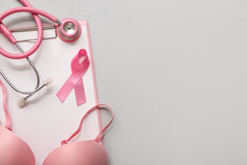 Pink ribbon with stethoscope, bra and clipboard on grey background. Breast cancer awareness concept