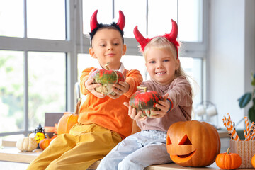 Fototapeta premium Little children with devil horns and Halloween pumpkins in kitchen