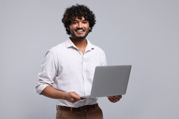 Smiling man with laptop on light grey background, space for text