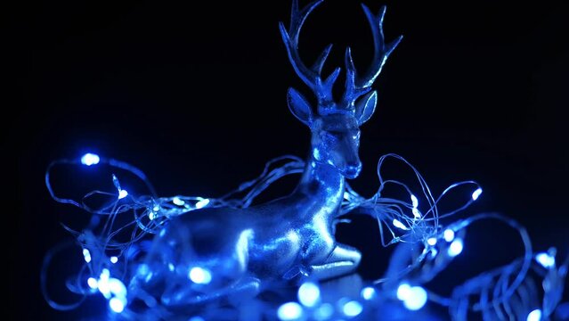 Christmas deer and garland on a dark background. Silver deer in blue flickering light in the dark. 4k footage