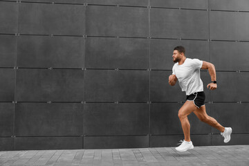 Young man running near building outdoors. Space for text