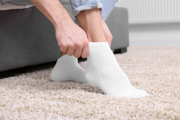 Man putting on white socks at home, closeup