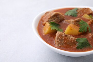 Delicious goulash in bowl on light grey table, closeup. Space for text