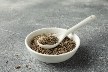 Bowl of caraway (Persian cumin) seeds and spoon on gray textured table