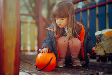 Fototapeta premium Little Girl with Halloween Candy Bucket Playing with a Cat. Child having fun outdoors with his pet going trick or treat 