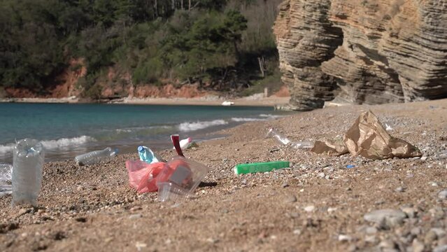 Picturesque beach with beautiful nature, garbage dump of plastic bottle, bag, paper is lying around. Environmental pollution. Vacationers left picnic waste trash by sea. Ecology, the danger of mankind