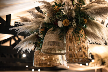 pampas grass and florals in wicker baskets hanging from black wooden beams at a wedding reception