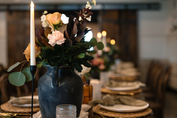 Wedding reception table with farmhouse elements and black vases with flowers and lit candles and...