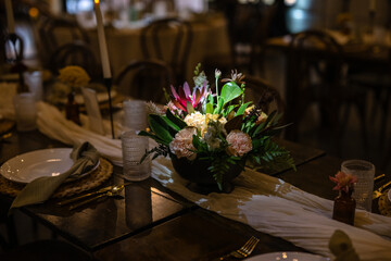 Wedding reception table with farmhouse elements and black vases with flowers and lit candles and...