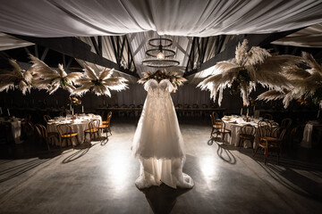 bride's gown hanging in reception venue with pampas grass in wicker baskets hanging from ceiling...