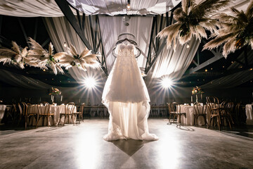 bride's gown hanging in reception venue with pampas grass in wicker baskets hanging from ceiling...