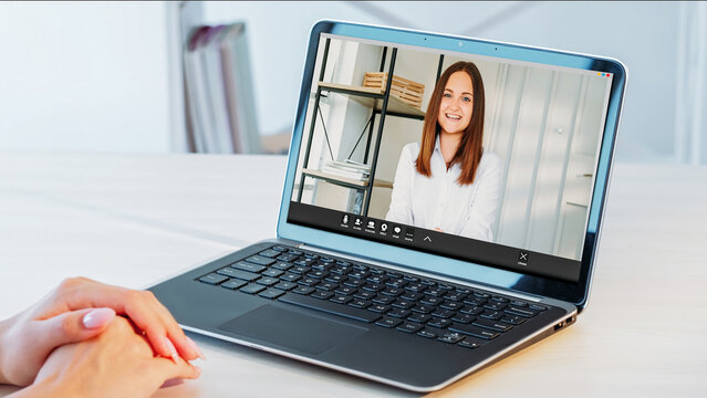 Virtual meeting. Video conference. Laptop with smiling business woman on screen and female hands at office desk at corporate online chat call.