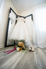 bridal gown hanging with flower girl dress with bouquet and bridal shoes in foreground