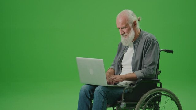 Green Screen.An Old Man in a Wheelchair Works on a Laptop.A Smart Elderly Man, Freelancer, Browsing on the Internet Using a Laptop and Shows Thumbs Up.Assistive Technologies for People in Wheelchairs.