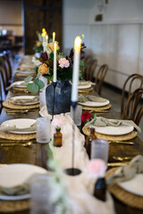 Wedding reception table with farmhouse elements and black vases with flowers and lit candles and place settings