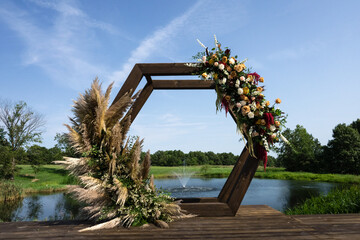 Fototapeta premium wedding arch with pampas and flowers adorning with a water founding in background