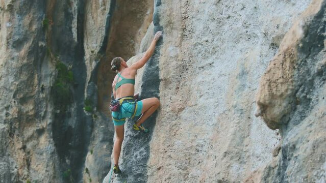 A young and strong woman is rock climbing on a rock. Strength and endurance.