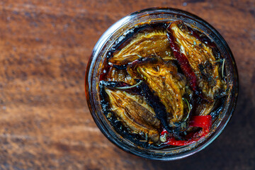 Sun-dried plums with garlic, green rosemary, red chili pepper, olive oil and spices in a glass jar on a wooden table. Rustic style, top view, closeup, copy space