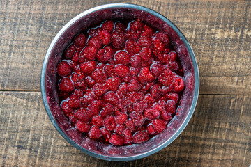 Fresh red raspberry berry, covered with granulated sugar for jam preparation in bowl, top view, closeup. Background and texture of raspberries with sugar
